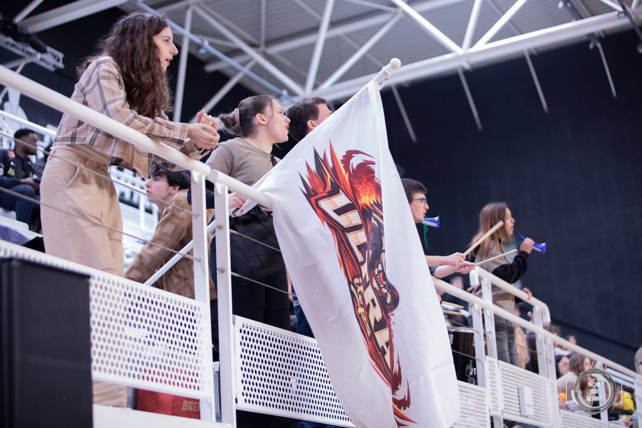 Une étudiante déploie un drapeau blanc frappé d'un blason par-dessus la rambarde des tribunes.