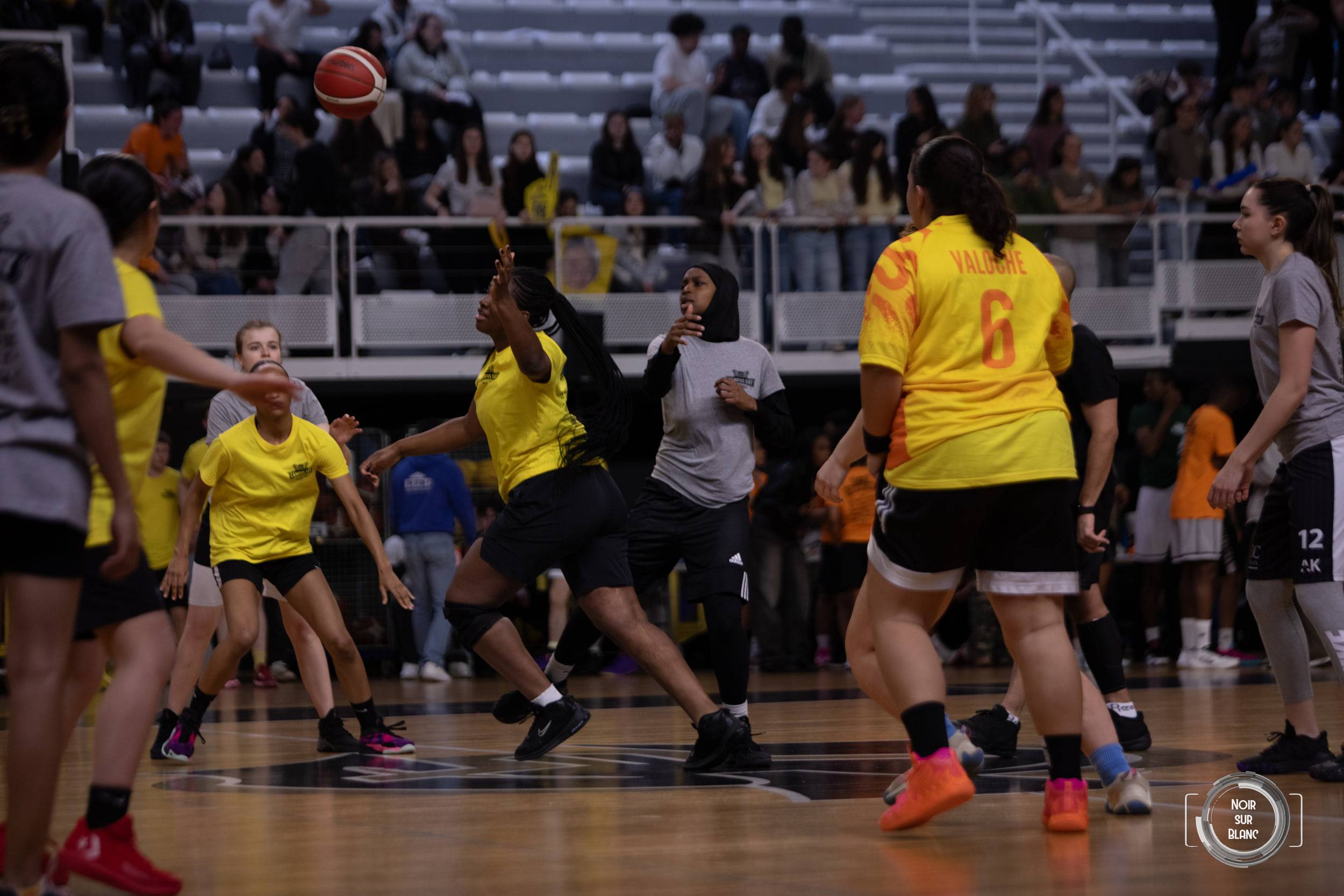 Match de basket entre une équipe en maillot jaune et une équipe en gris, le ballon en l'air au-dessus de la raquette.
