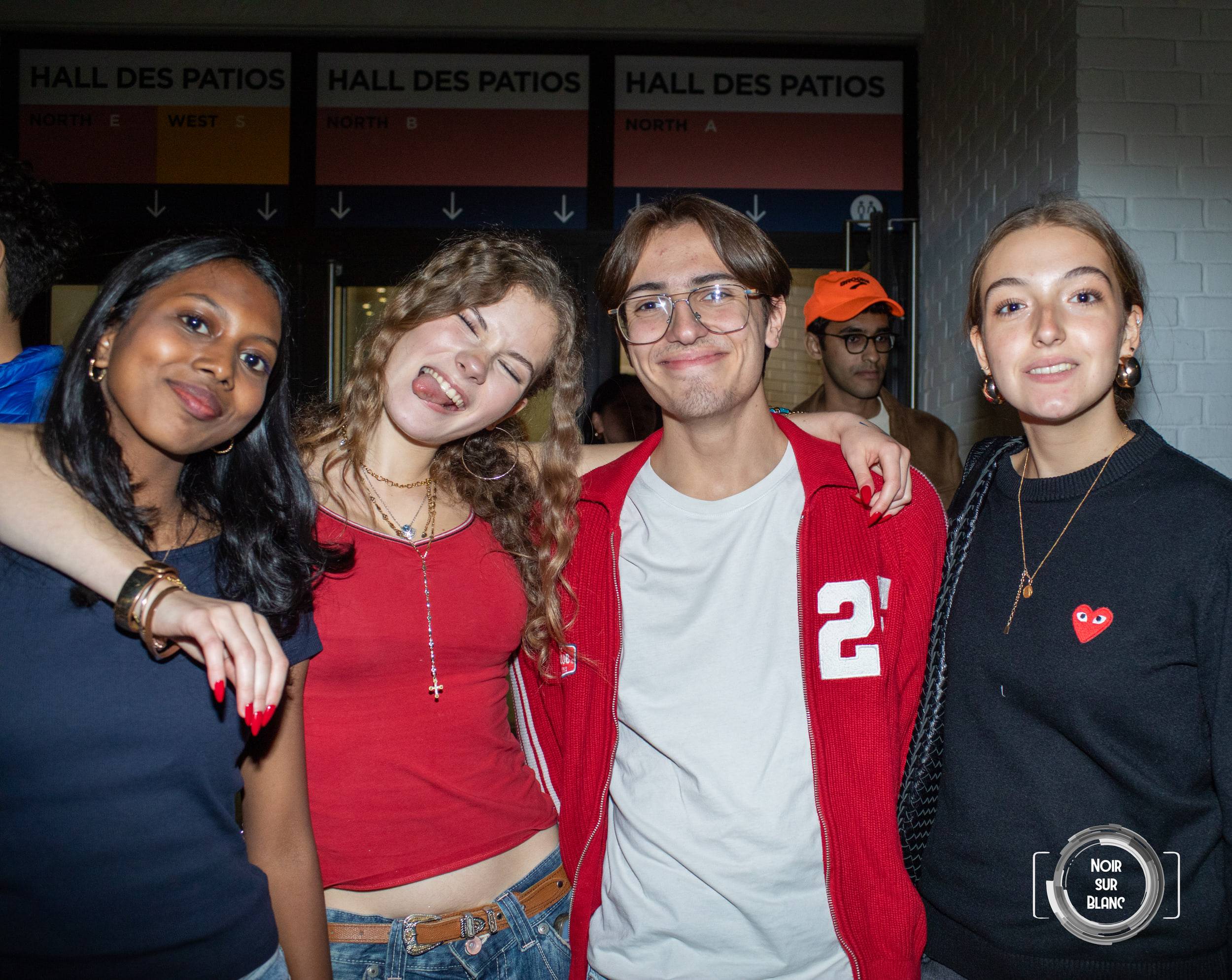 Quatre étudiants posent épaule contre épaule devant trois panneaux marqués « Hall des Patios ».