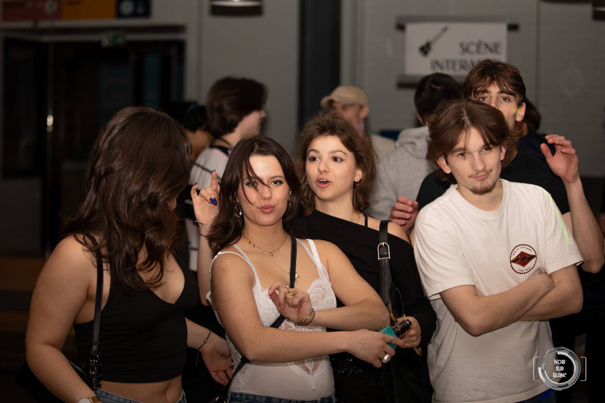 Un groupe d'étudiants pose en souriant dans un hall, devant un panneau « Scène internationale » accroché au mur.