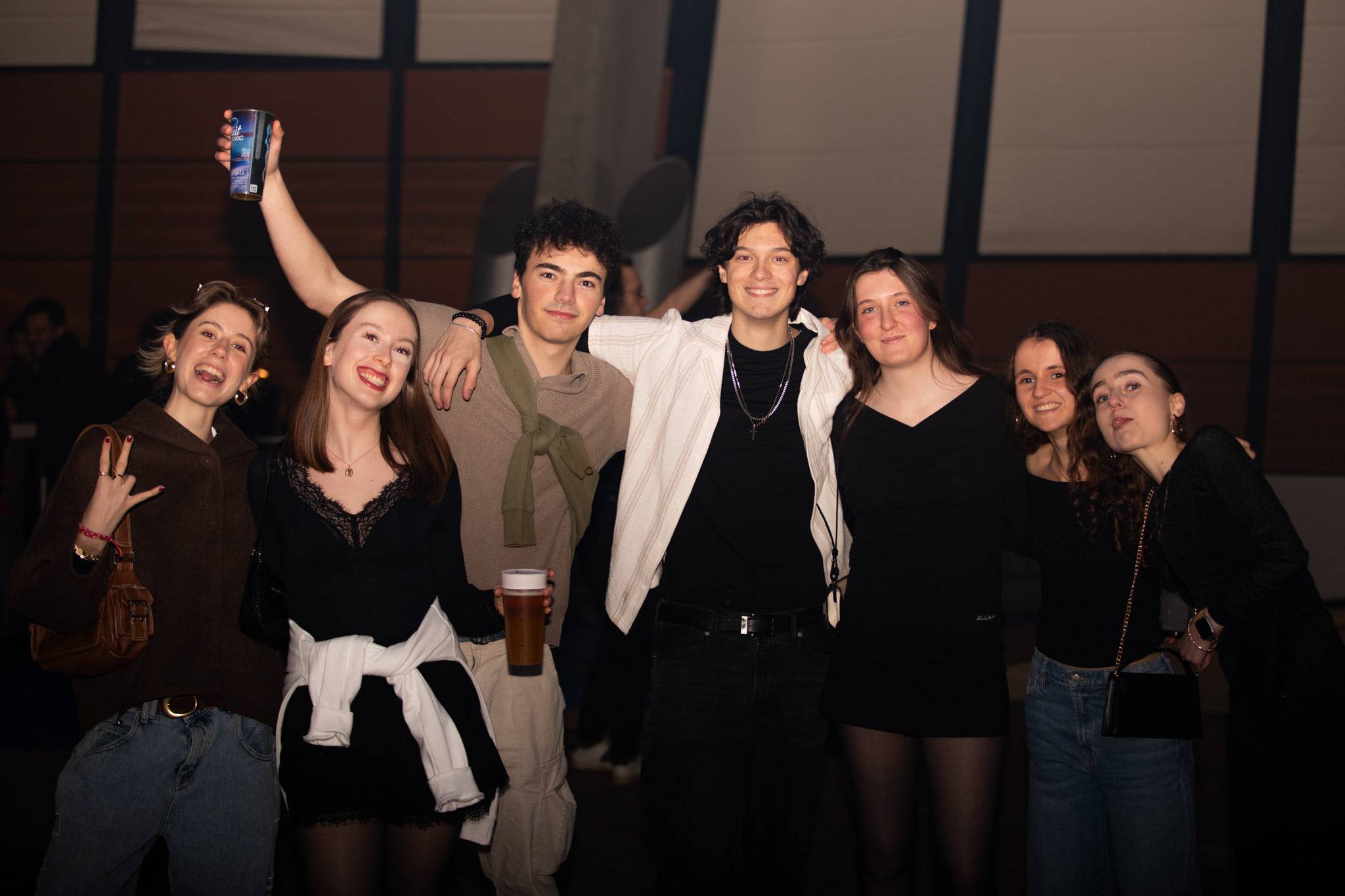 Sept étudiants en tenue sombre posent épaule contre épaule dans un hall, l'un d'eux brandissant son téléphone au-dessus du groupe.