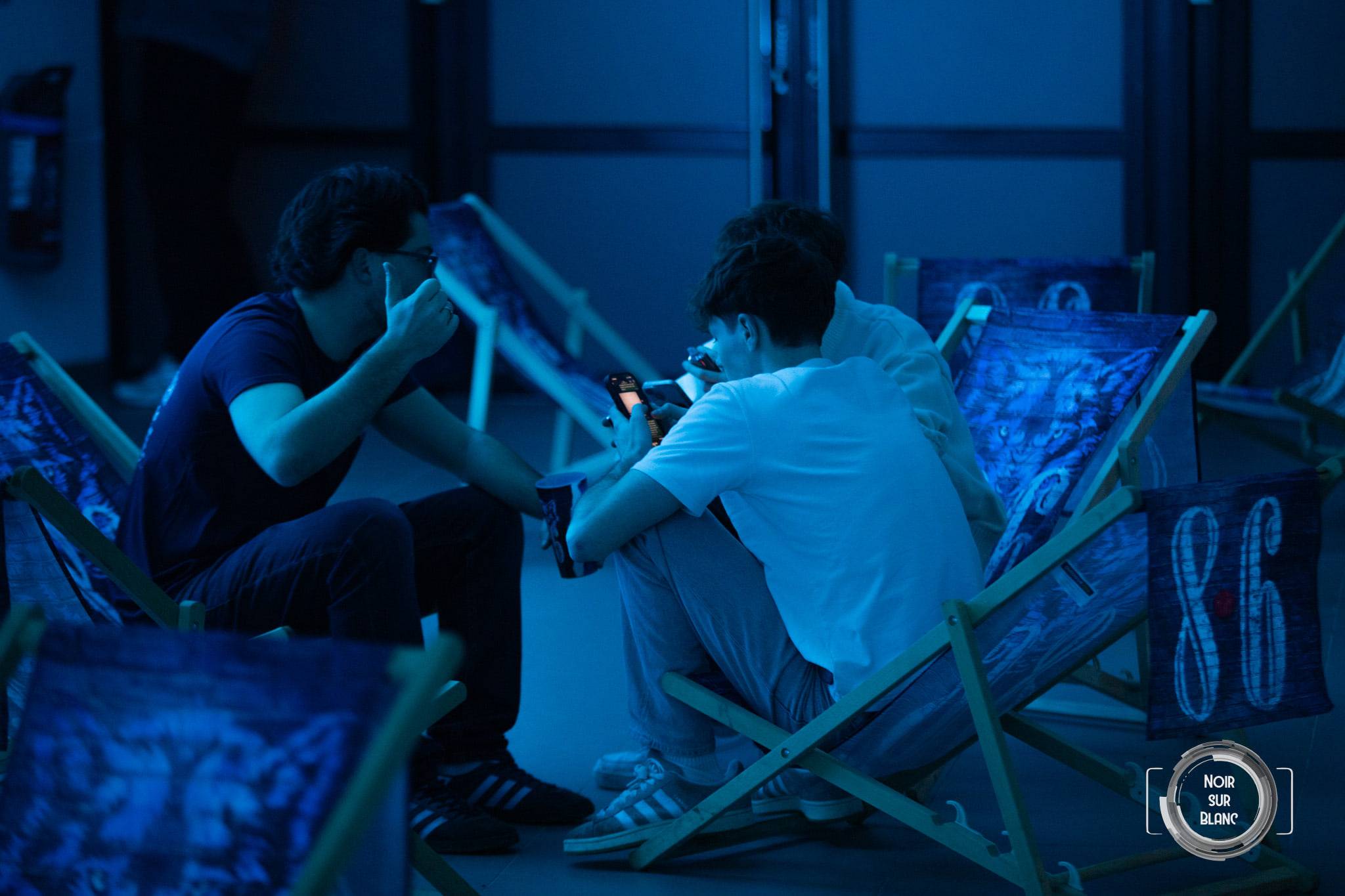 Deux étudiants affalés dans des transats consultent leur téléphone, baignés dans une lumière bleue.