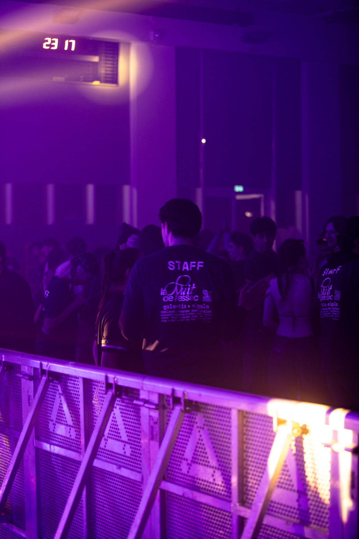 Un membre du staff de dos face à la piste, son sweat marqué « la Nuit de l'ESSEC », dans une lumière violette.