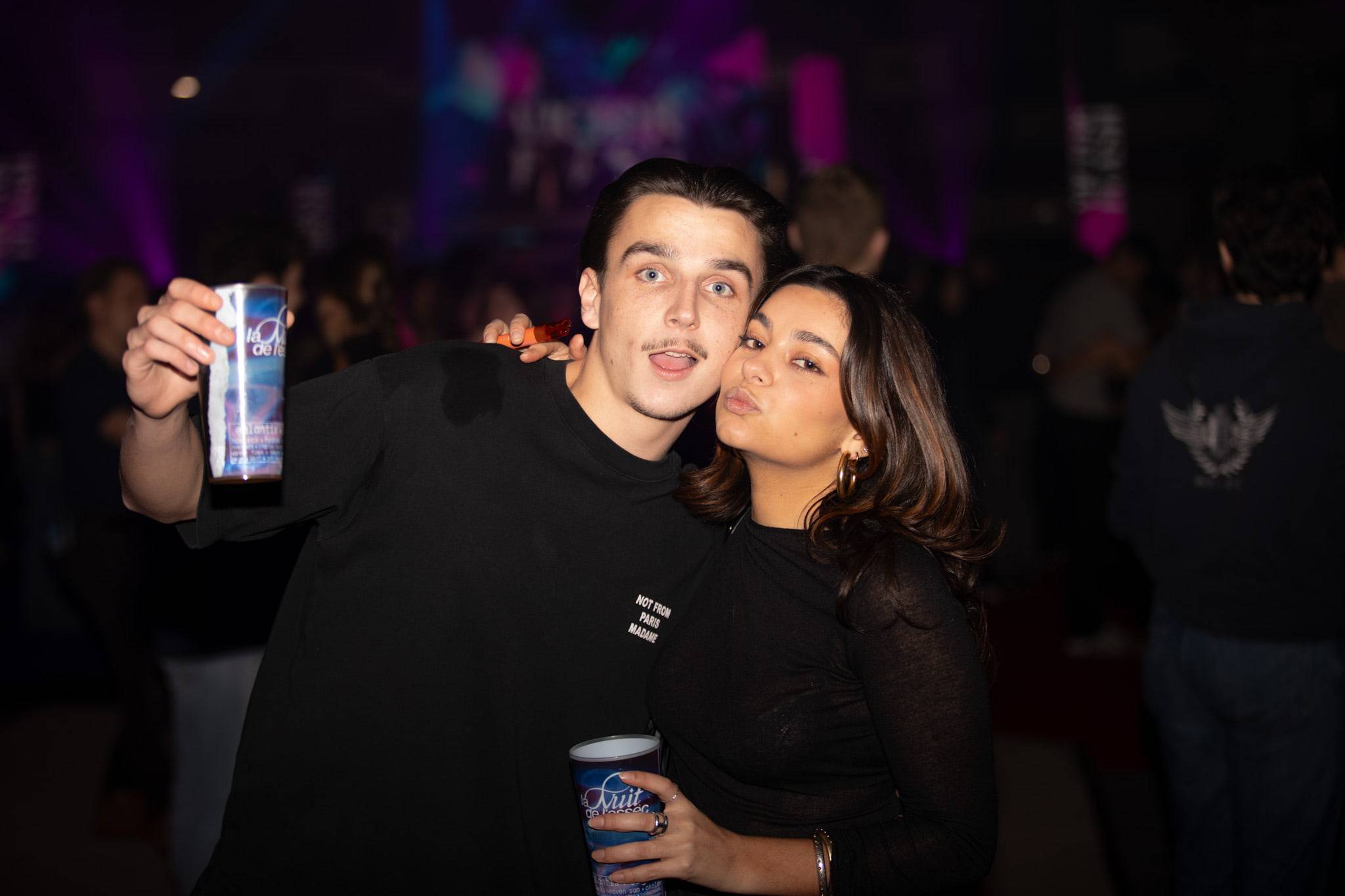 Deux étudiants posent joue contre joue, l'un brandissant un gobelet au logo de la soirée.