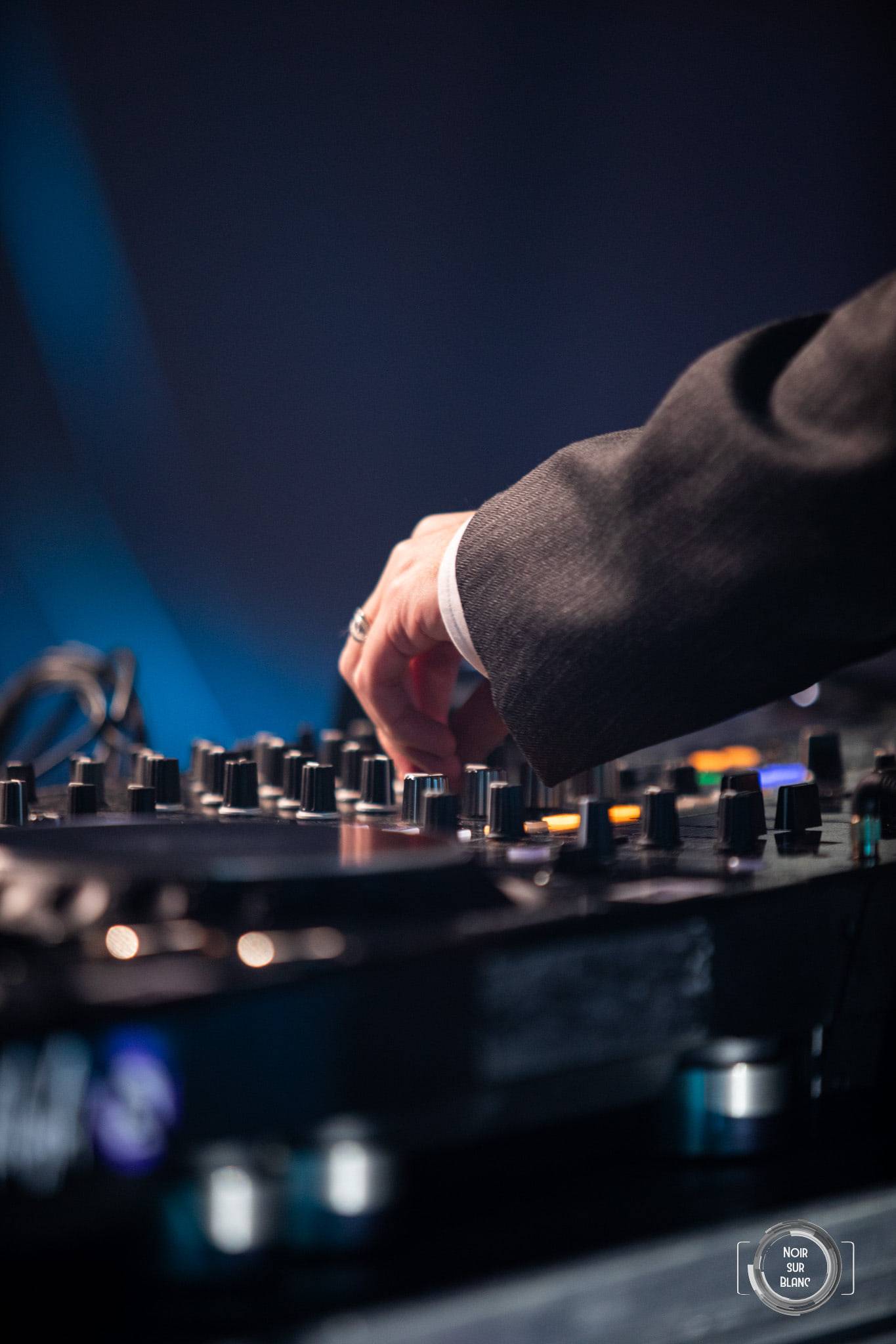 Gros plan sur une main qui règle les potentiomètres d'une table de mixage, dans une lumière bleue.