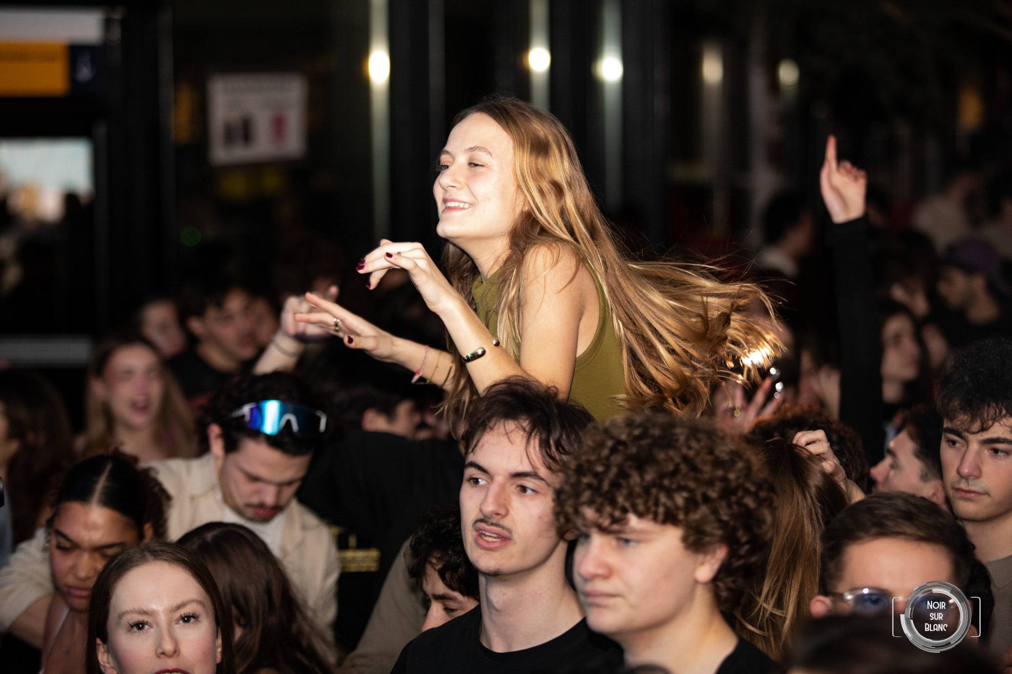Une étudiante juchée sur des épaules, cheveux au vent, au milieu d'une foule compacte.