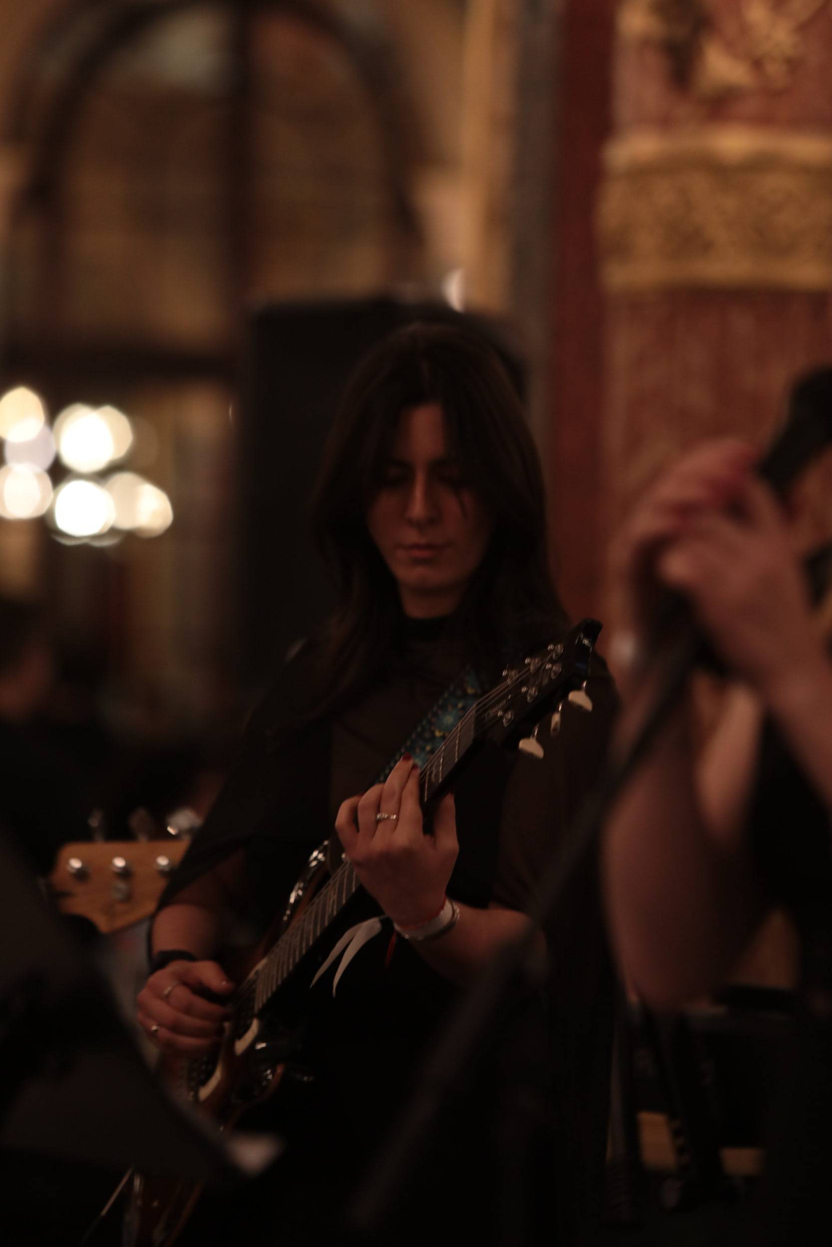 Une guitariste joue au milieu des dorures et des lustres d'une salle de bal, éclairée de côté.