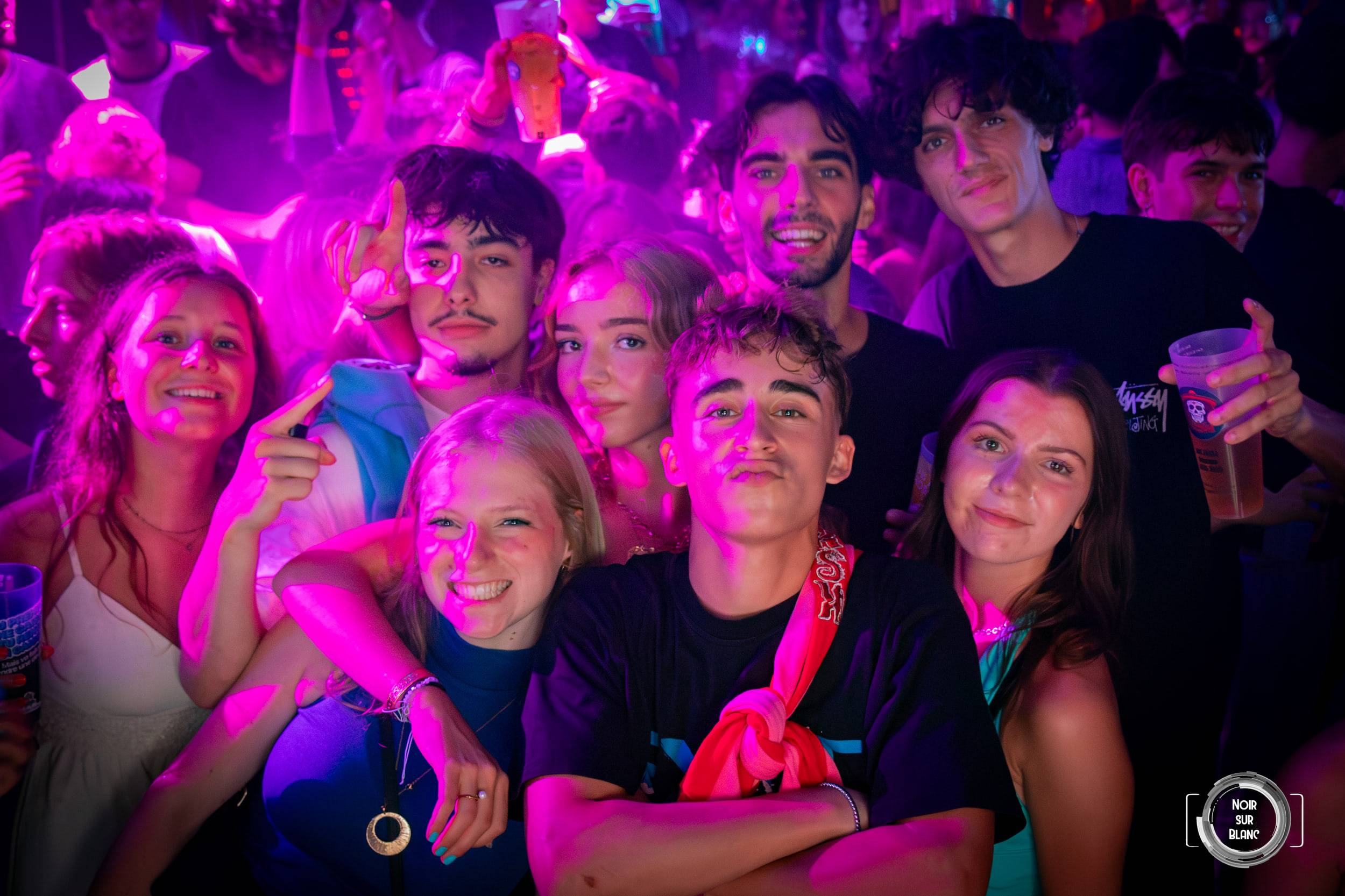 Une dizaine de visages serrés les uns contre les autres face à l'objectif, sous une lumière magenta, gobelets à la main.