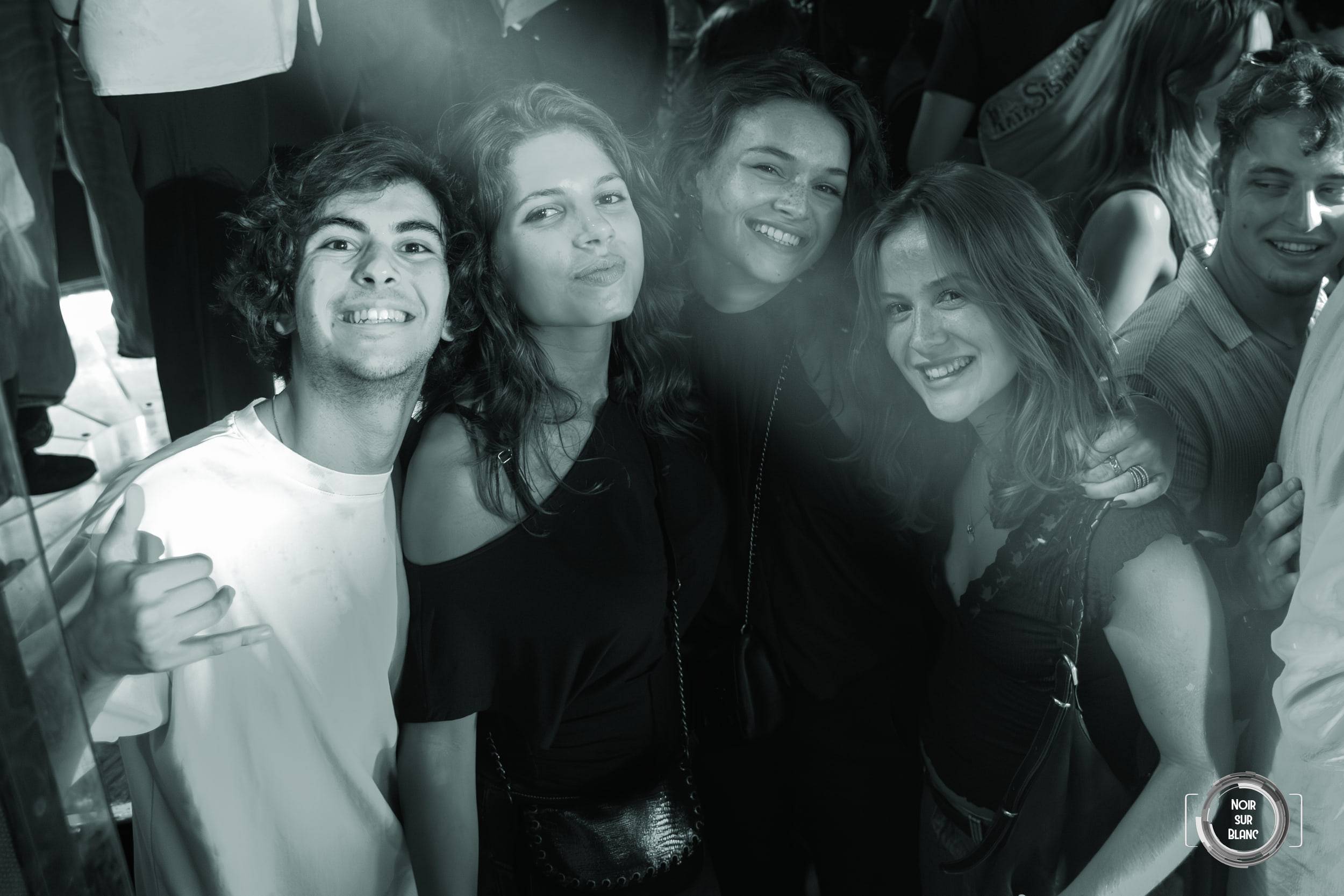 Photo en noir et blanc : cinq amis serrés les uns contre les autres, souriant à l'objectif au milieu de la foule.