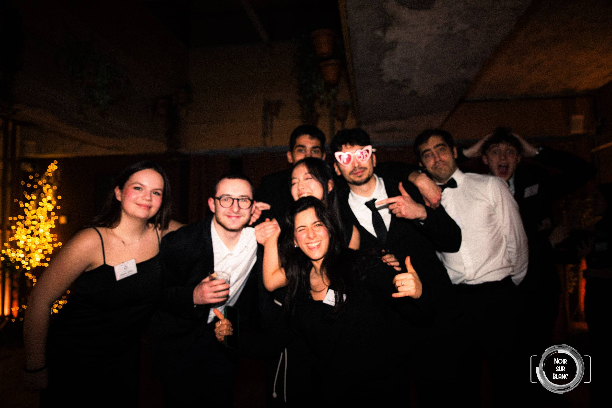 Une dizaine d'invités se serrent pour la photo, certains en lunettes en forme de cœur, devant un arbre couvert de guirlandes.