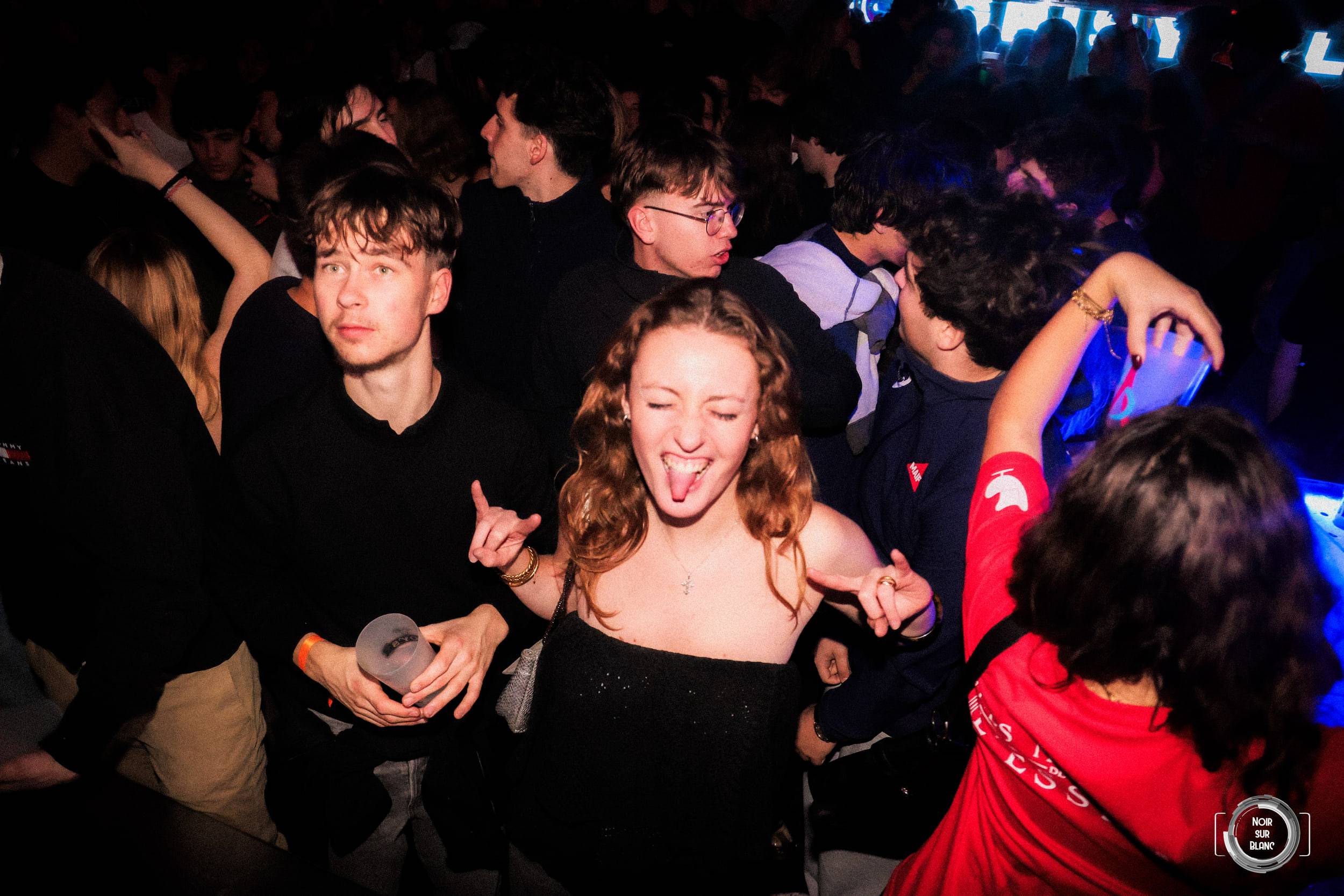 Au milieu des danseurs, une jeune femme tire la langue vers l'objectif, un gobelet à la main.