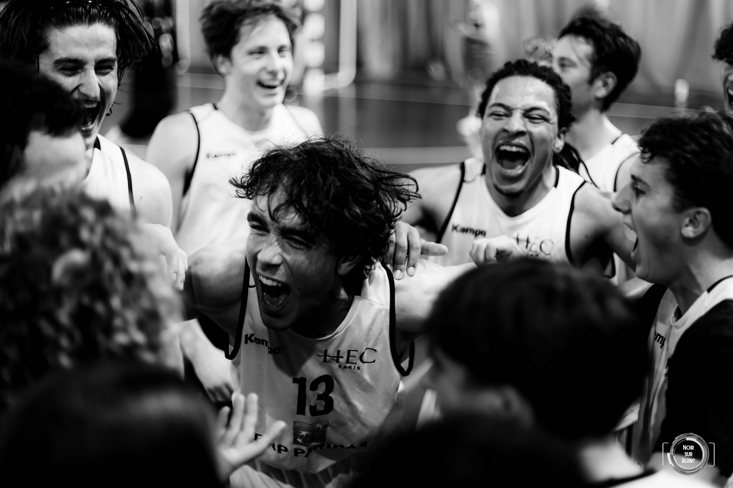 Serré au milieu de ses coéquipiers en maillot blanc, un basketteur hurle sa joie après le coup de sifflet final.