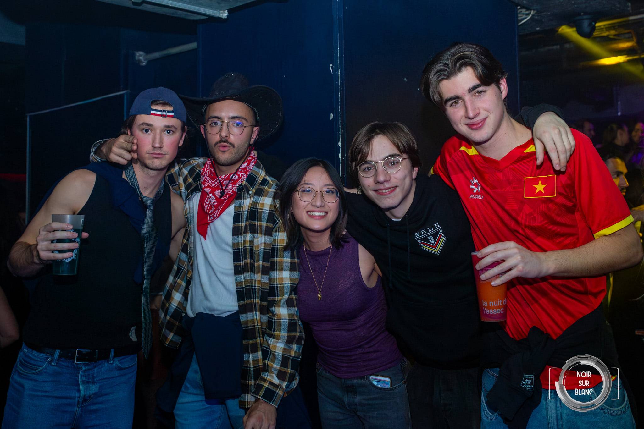 Un groupe pose en costumes dépareillés : chapeau de cow-boy, bandana rouge, maillot de football.