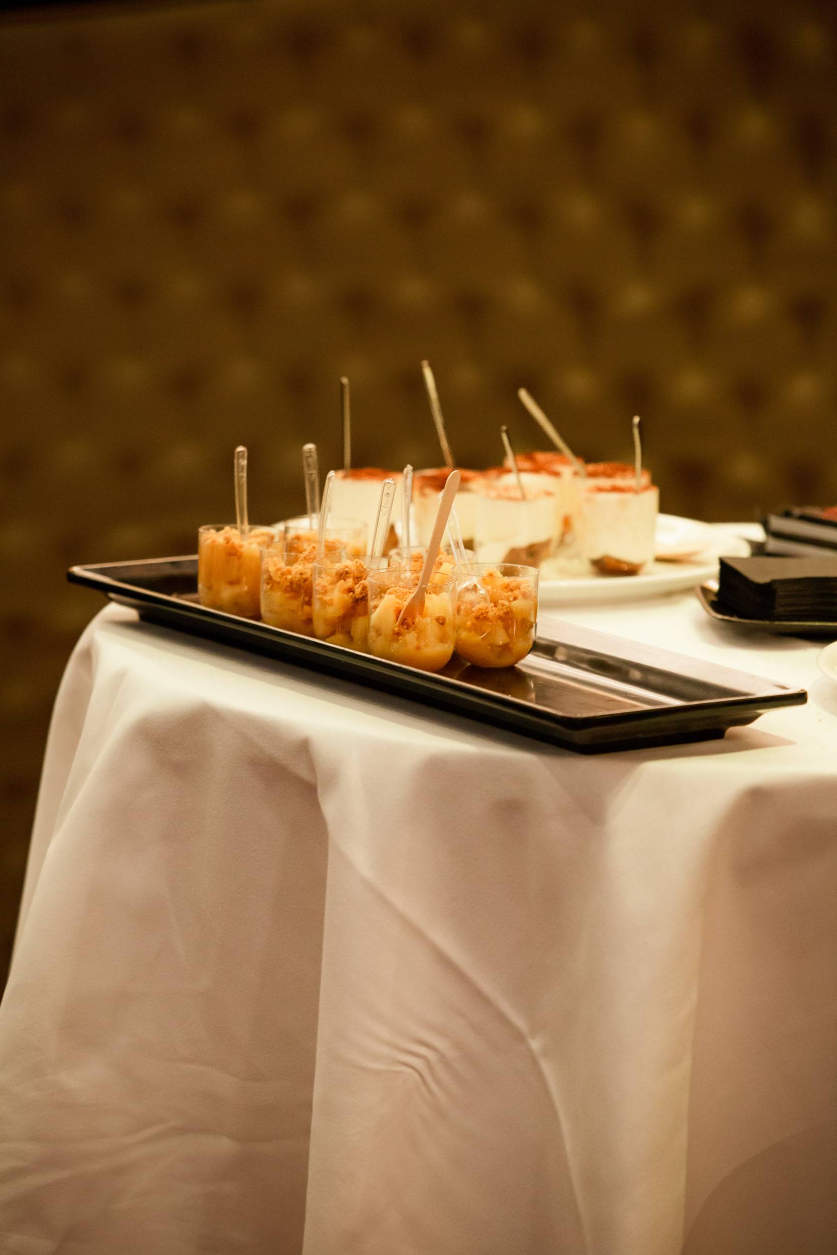 Un plateau de petits fours piqués de pics en bois, posé sur une table drapée de blanc devant une tenture dorée.