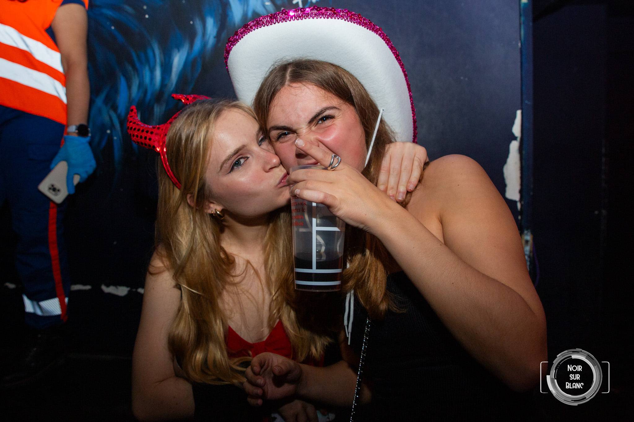 Deux amies joue contre joue, l'une sous un chapeau de cow-boy blanc, l'autre coiffée de cornes de diable rouges.