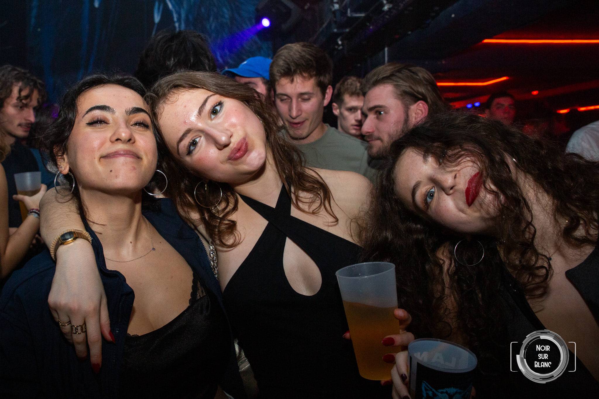 Un groupe de jeunes femmes pose verre à la main, l'une d'elles du faux sang au coin des lèvres, dans les néons rouges du club.