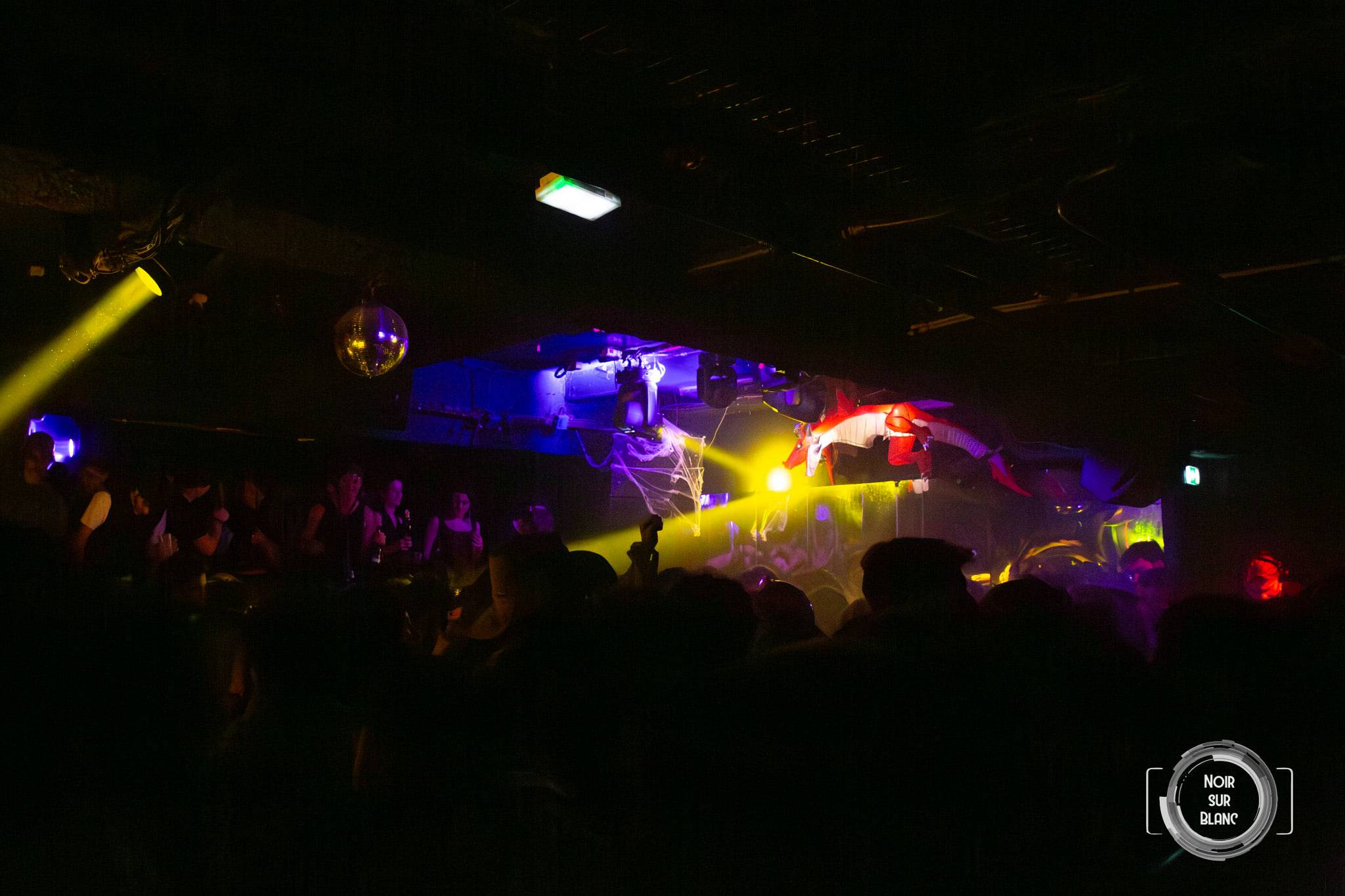 Vue du fond du club : la cabine du DJ n'est plus qu'une tache de lumières colorées au bout d'une salle noire.