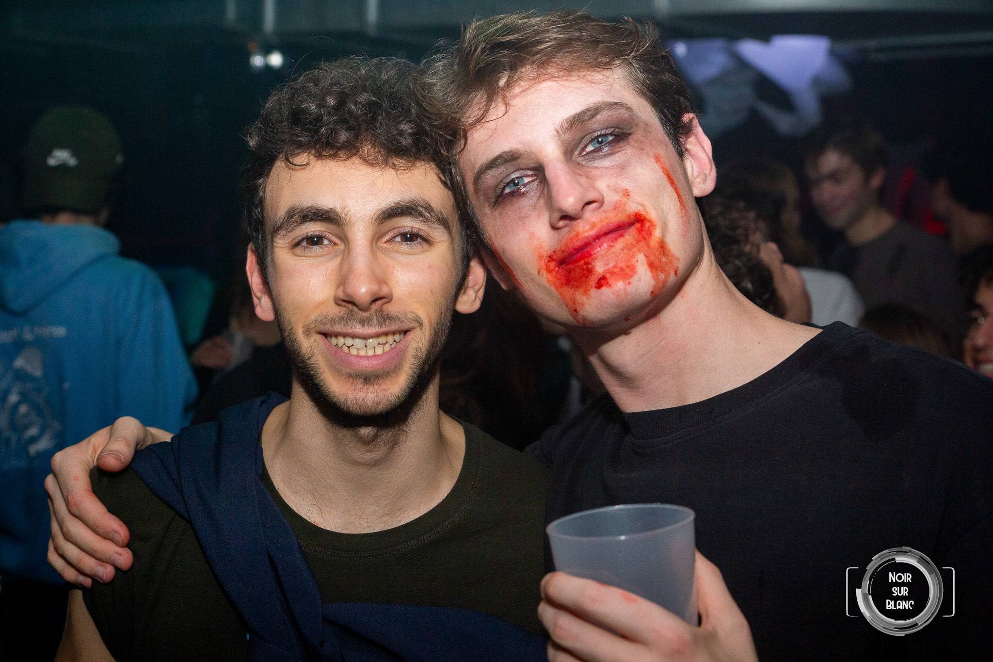 Deux garçons posent bras dessus bras dessous, l'un maquillé en mort-vivant avec du faux sang à la bouche, gobelet à la main.
