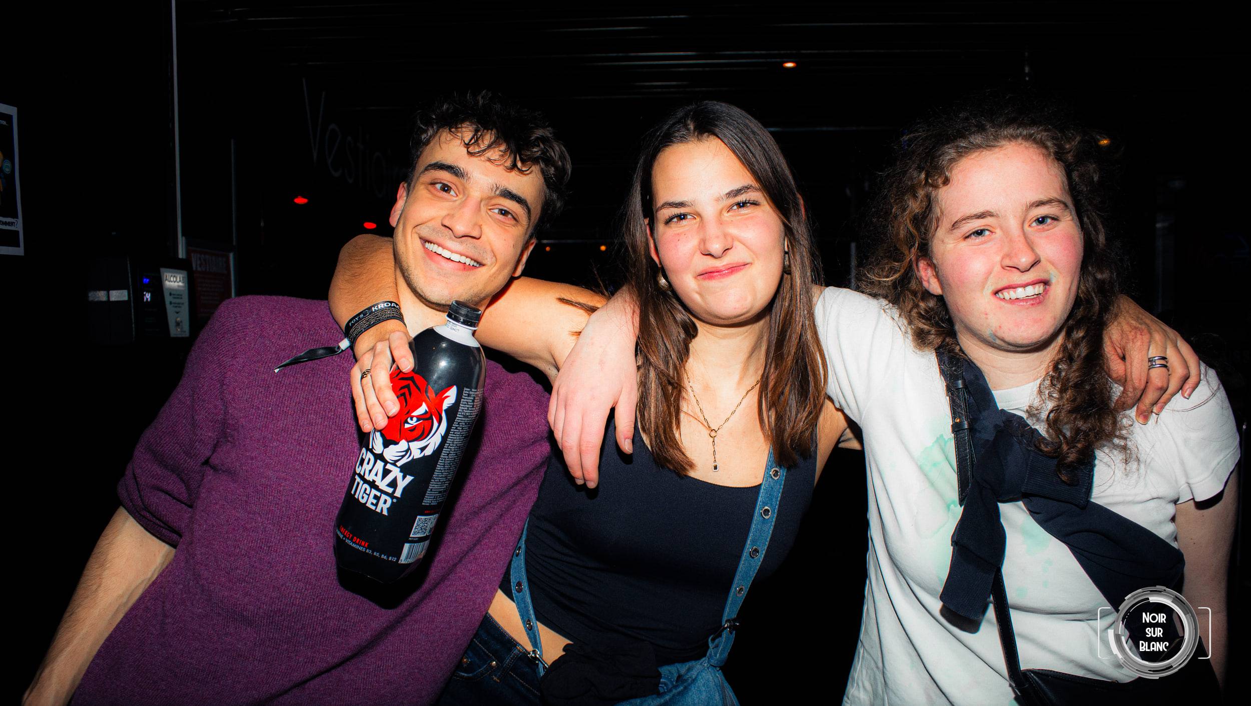 Trois amis bras dessus bras dessous posent dans le noir du club, l'un d'eux tient une canette de boisson énergisante.