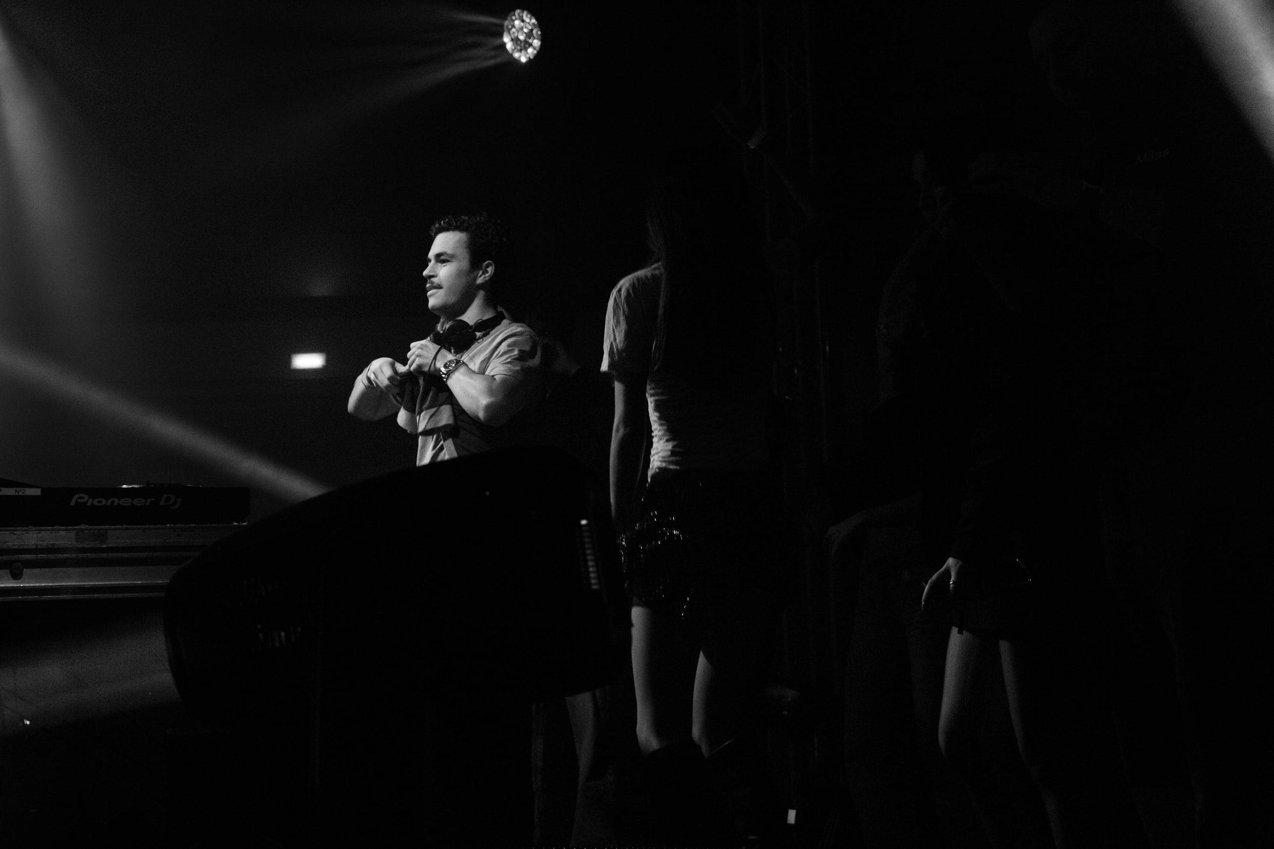 Photographie en noir et blanc d'un chanteur au micro dans un halo de lumière, le public en silhouette autour de lui.