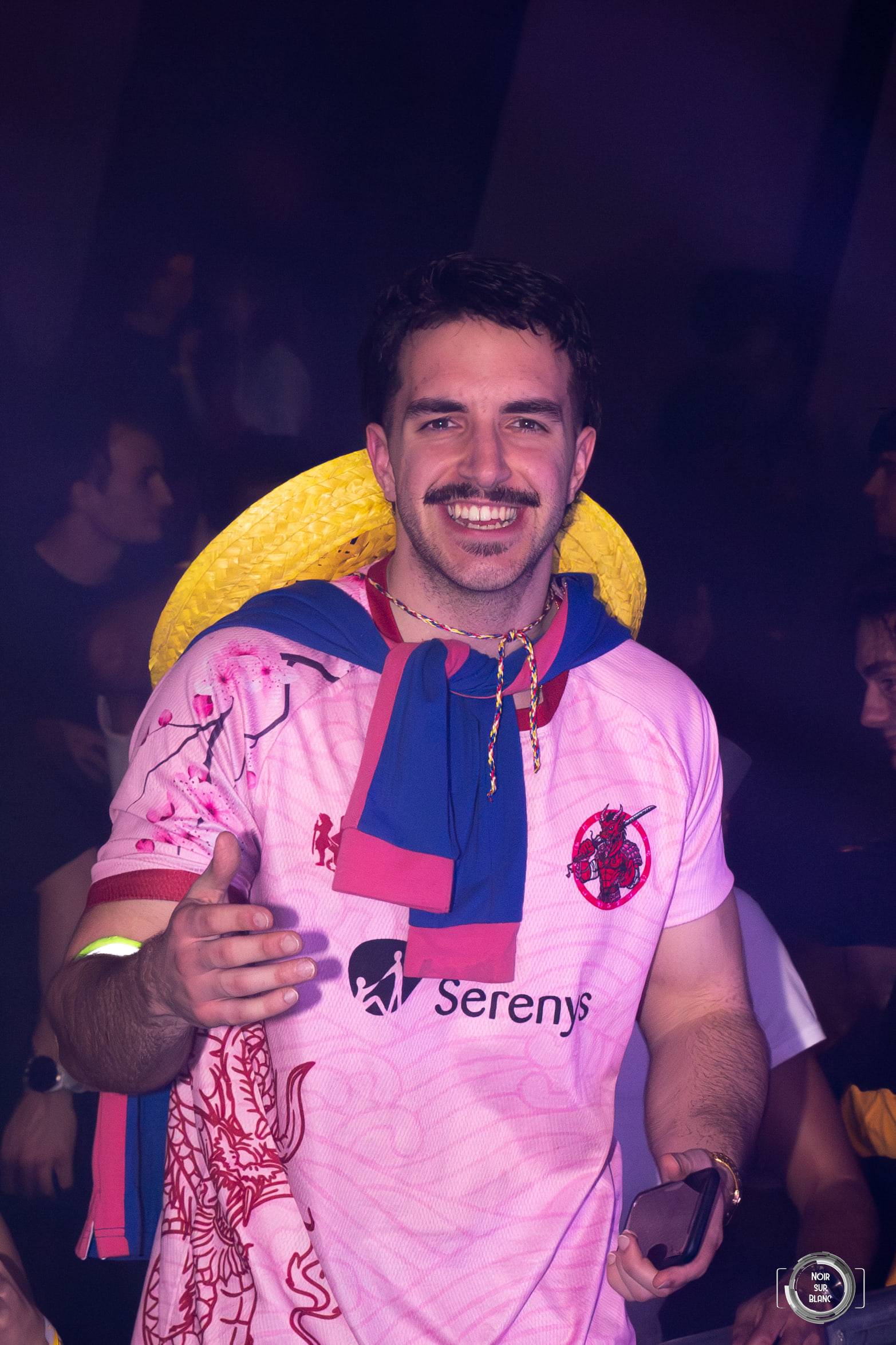 Un étudiant en maillot de rugby rose pose bras ouverts au milieu de la foule.