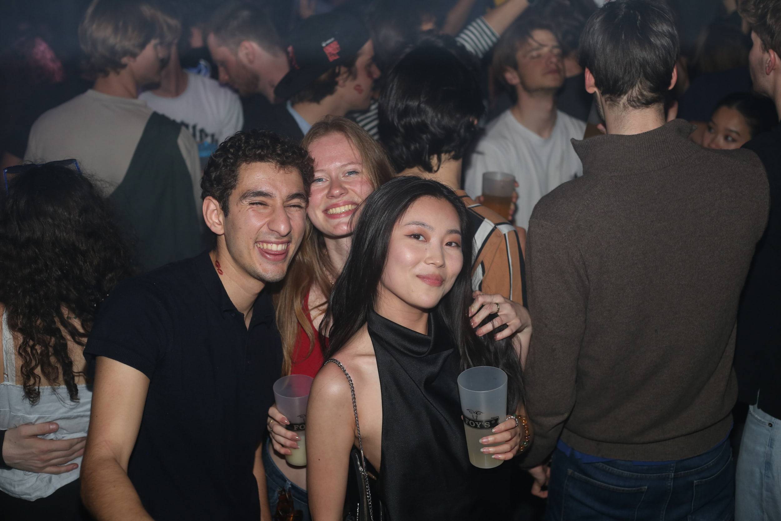 Trois amis posent gobelets à la main au milieu de la foule qui danse.