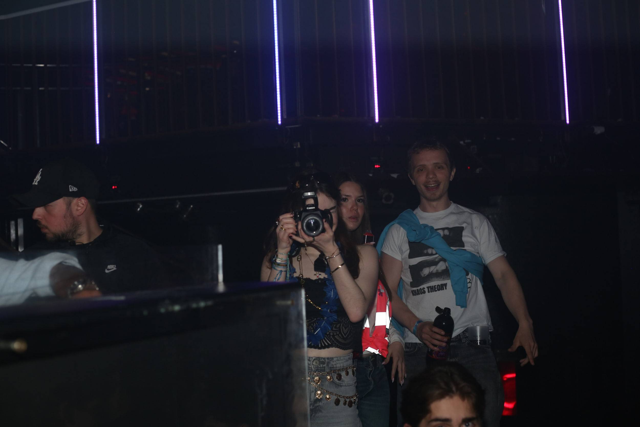 Une photographe déclenche son flash en direction de l'objectif, deux amis posant à ses côtés.