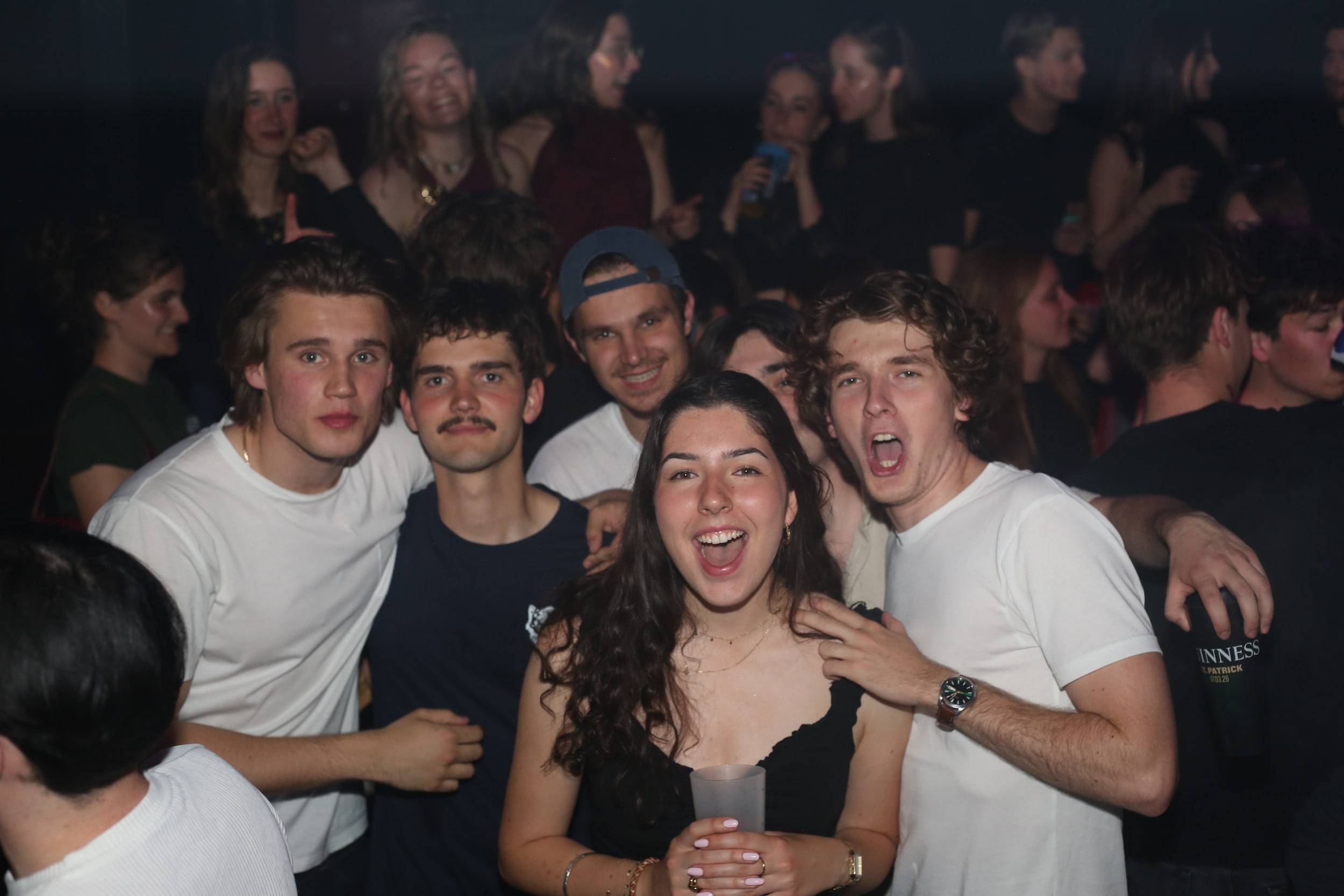 Un groupe hilare pose bras autour des épaules au milieu de la foule du club.