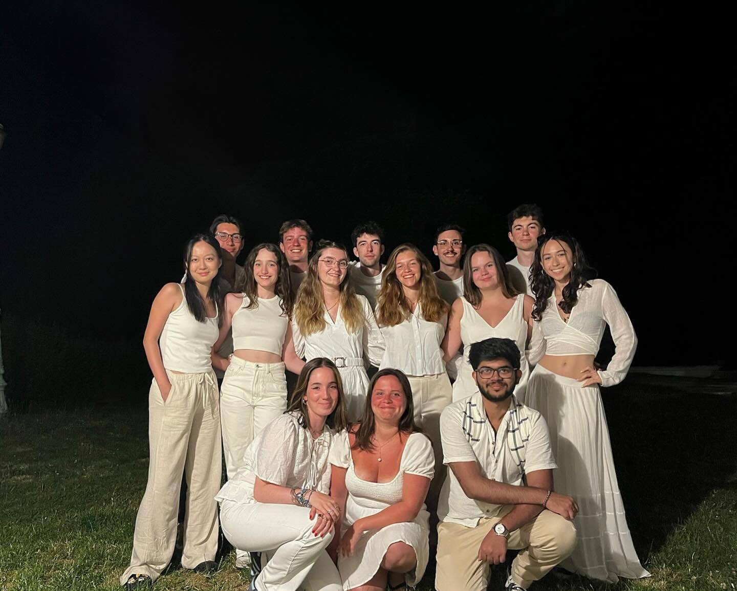 Une quinzaine d'étudiants habillés tout en blanc posent en groupe sur une pelouse, de nuit.