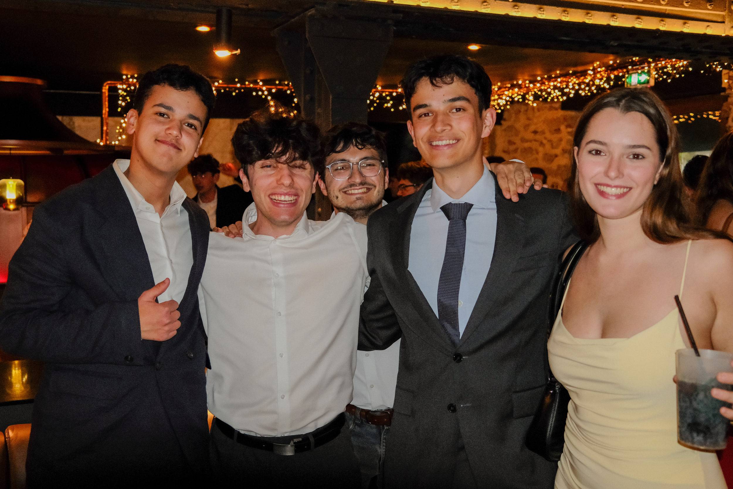 Cinq étudiants en tenue de soirée posent serrés les uns contre les autres, l'un d'eux levant le pouce.