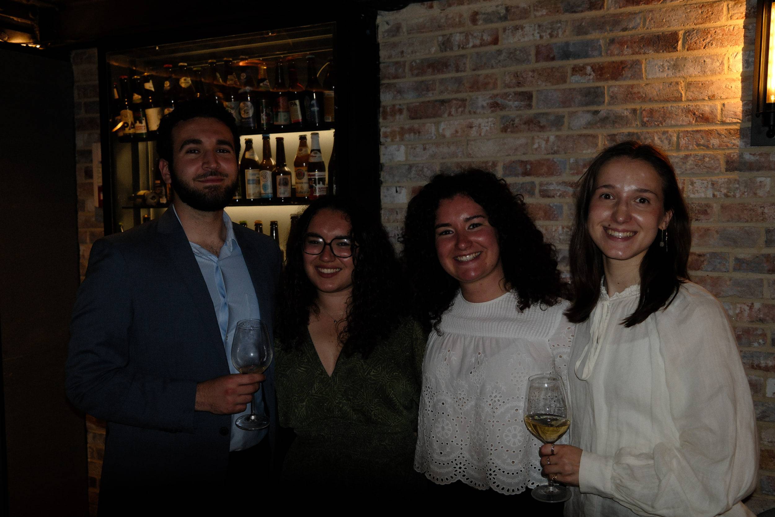 Quatre étudiants, verres de vin à la main, posent devant la vitrine du bar.