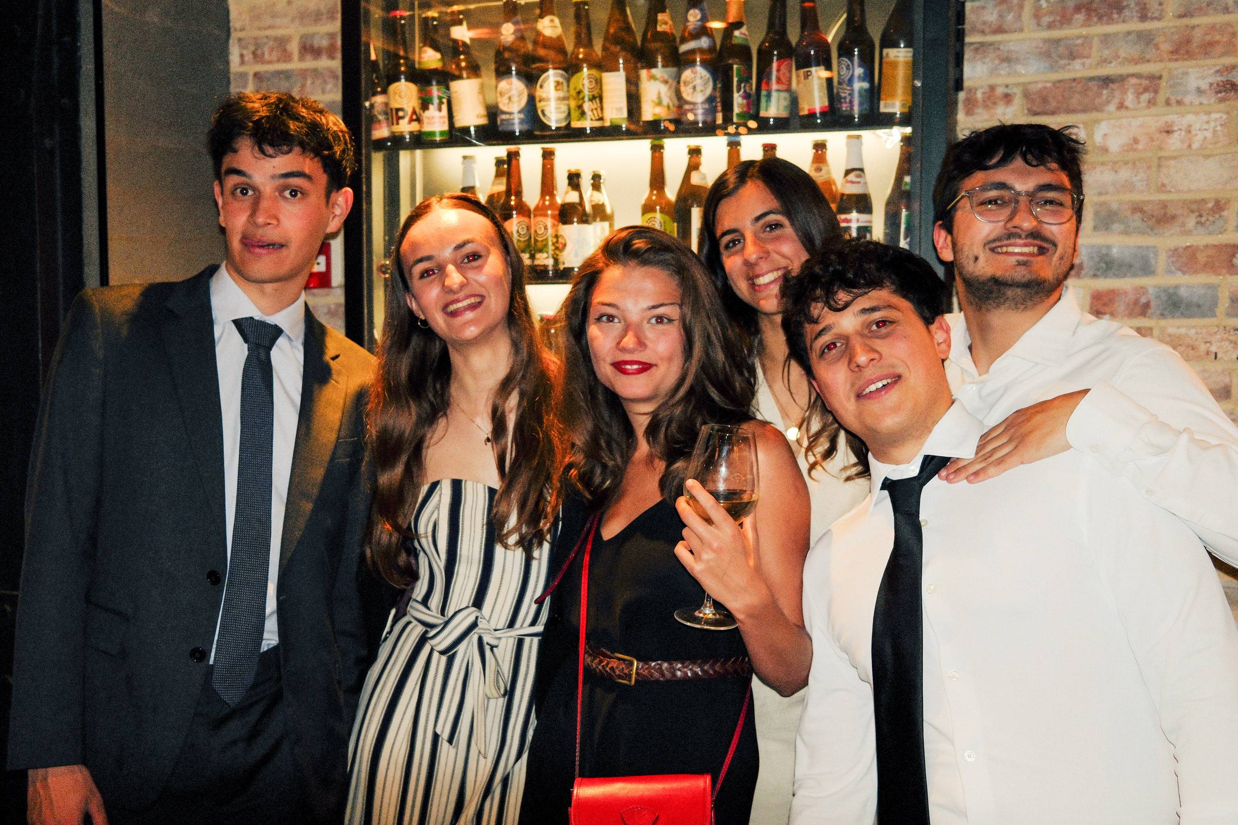 Six étudiants serrés devant la vitrine à bouteilles, l'un d'eux penché au premier plan.