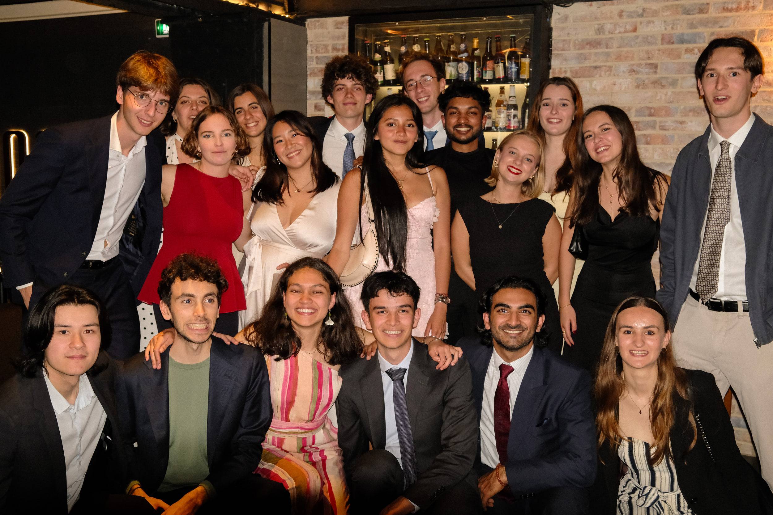 Une vingtaine d'étudiants en tenue de soirée posent sur deux rangs, les premiers accroupis devant le bar.
