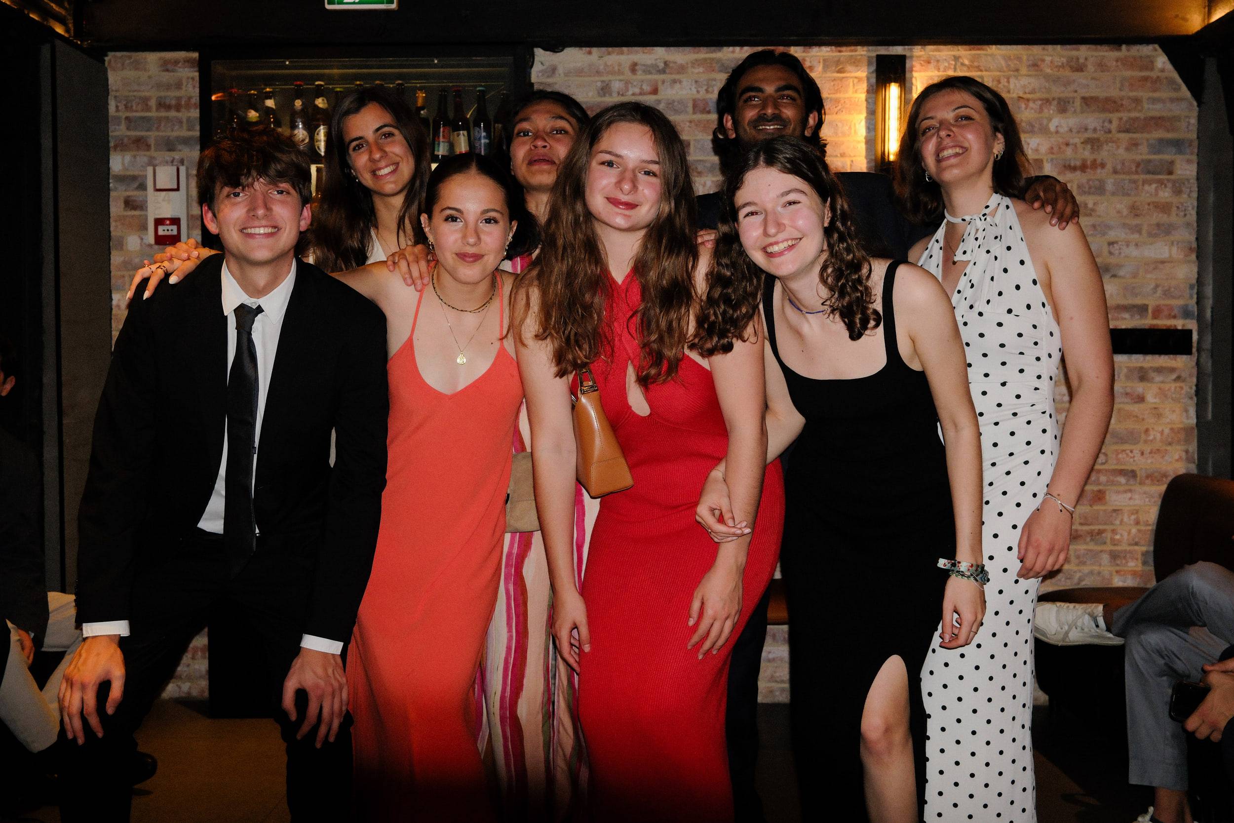 Sept étudiants posent devant le bar, plusieurs en robe longue rouge, noire ou blanche.