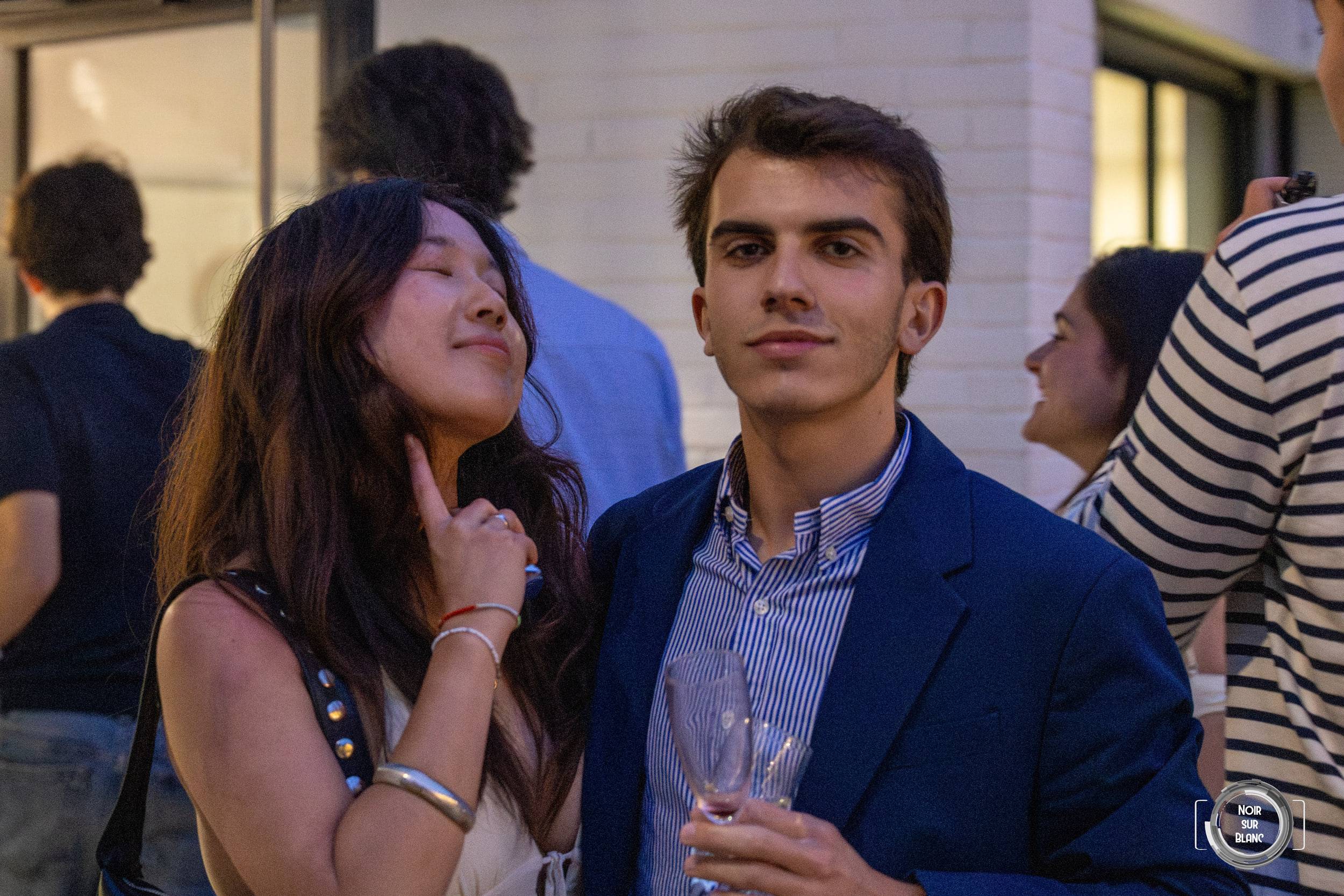 Une invitée pose la main sous son menton en regardant un invité en costume bleu, une coupe de champagne à la main.