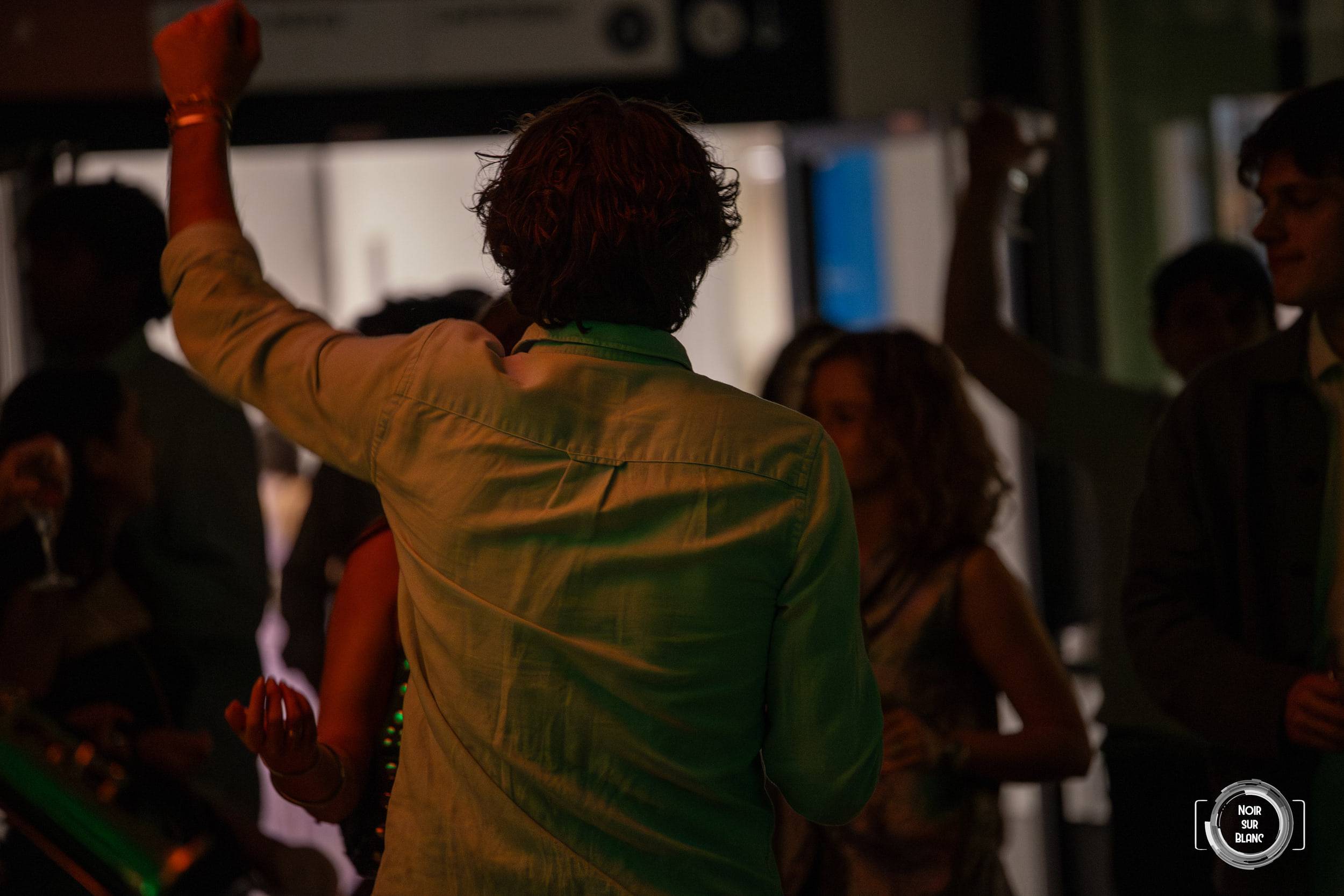 Un danseur de dos lève le poing face aux musiciens, la piste éclairée en vert derrière lui.