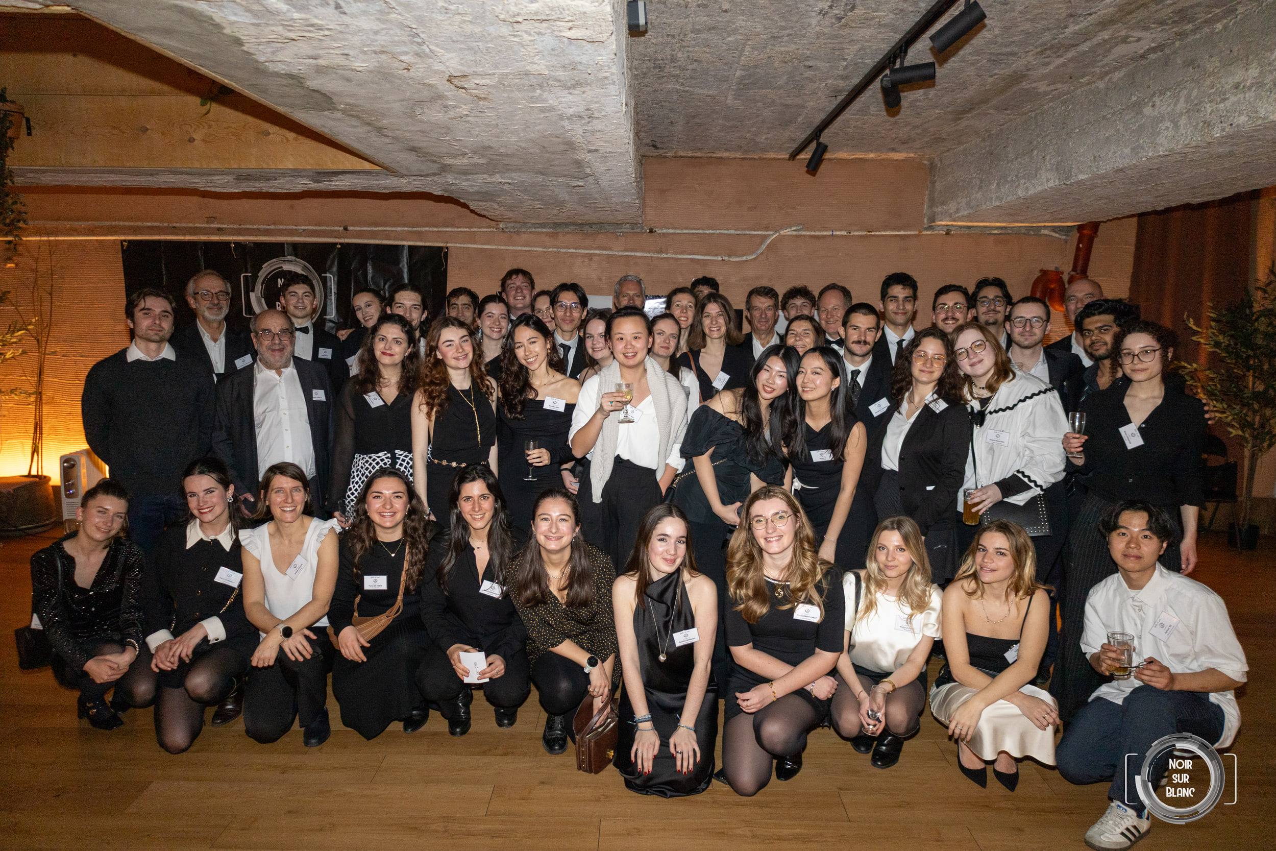 Une cinquantaine de membres de l'association posent en groupe, debout et accroupis, sous les poutres de béton de la salle du gala.