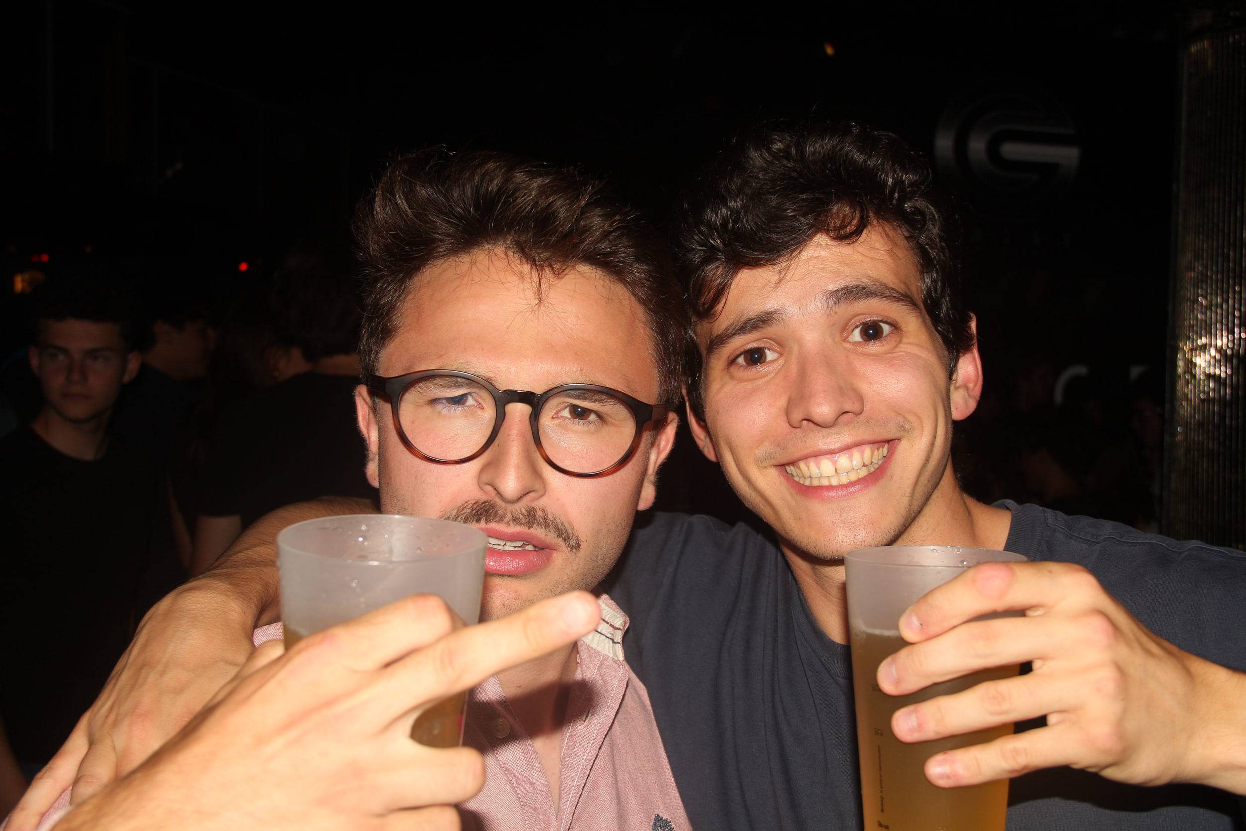 Deux amis tendent leurs gobelets vers l'objectif en souriant, la foule derrière eux.