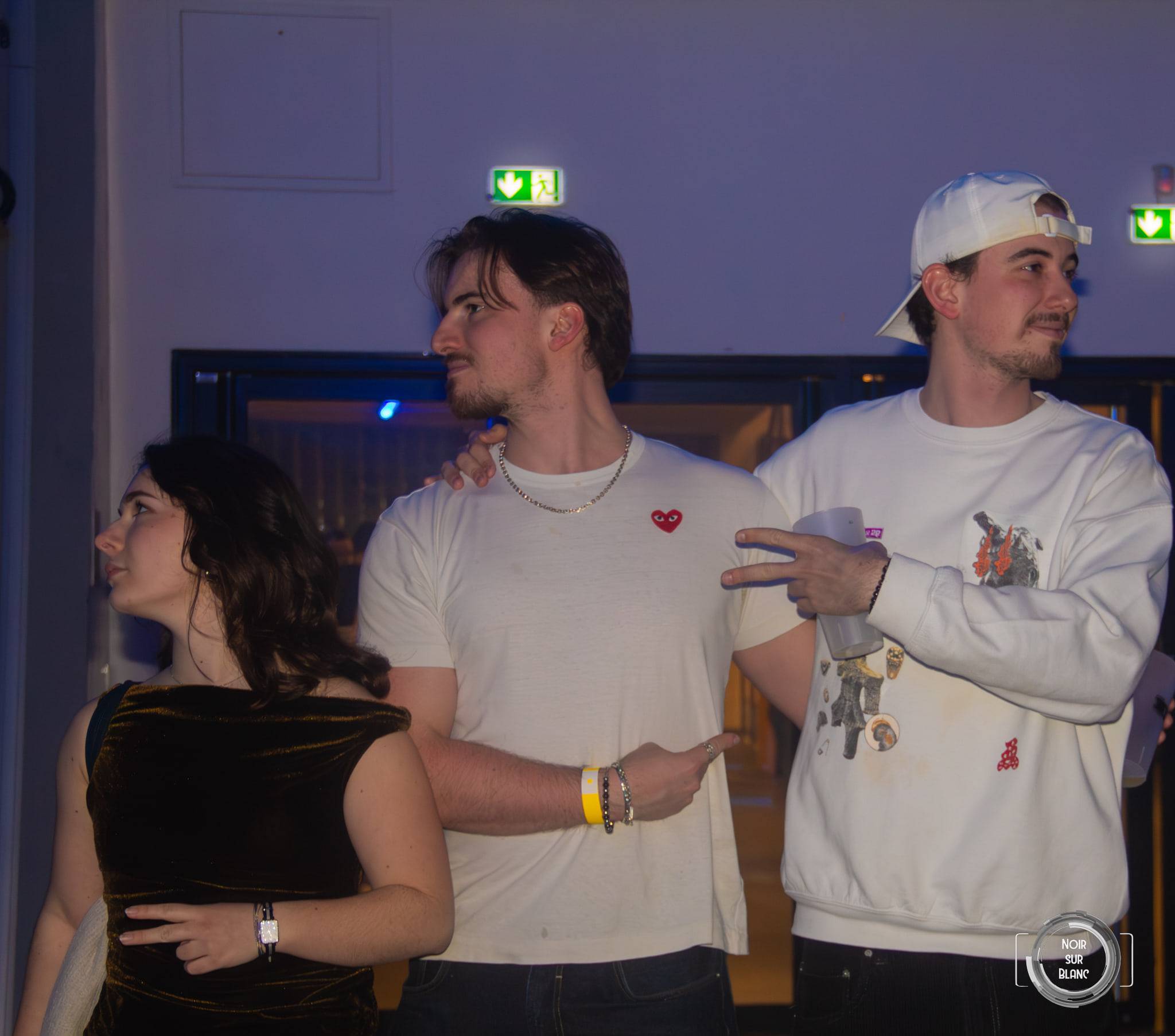 Trois étudiants posent près de l'entrée de la salle, l'un d'eux en casquette blanche portée à l'envers.