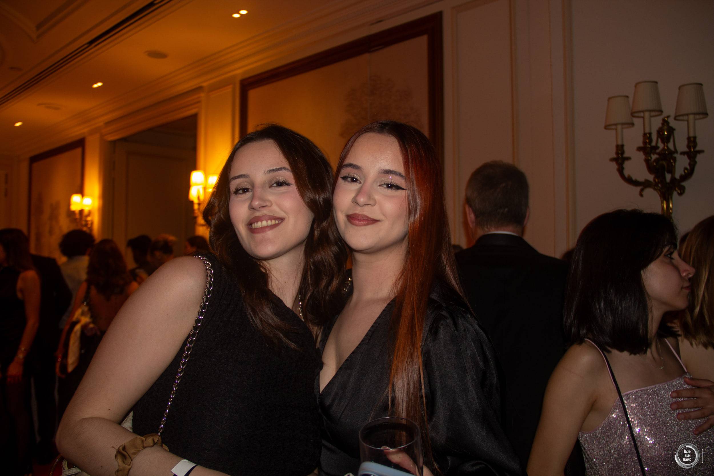 Deux étudiantes posent côte à côte dans un salon aux appliques dorées, tard dans la soirée.