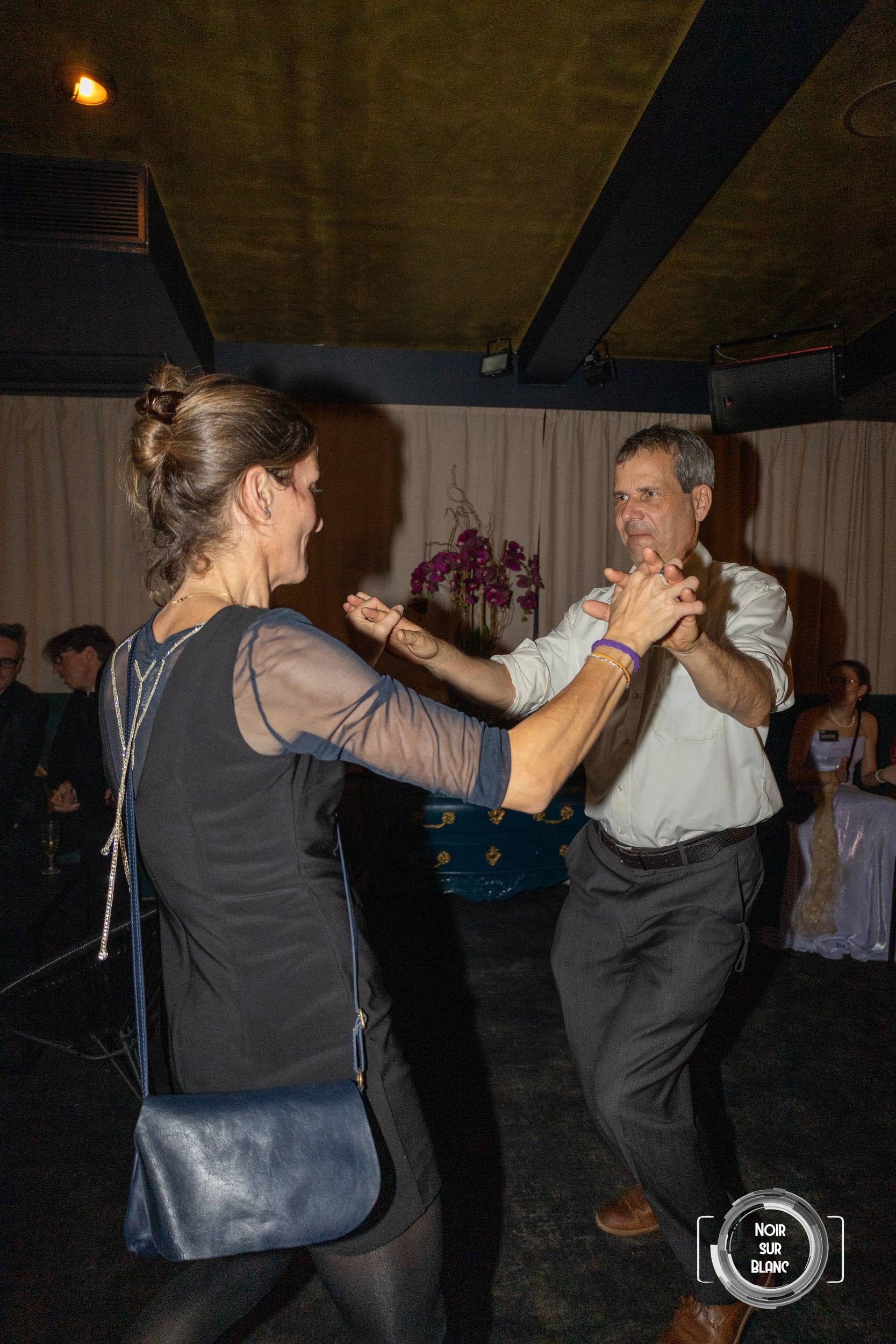 Un couple danse au milieu de la salle, les mains jointes, sous la lumière rasante d'une soirée.