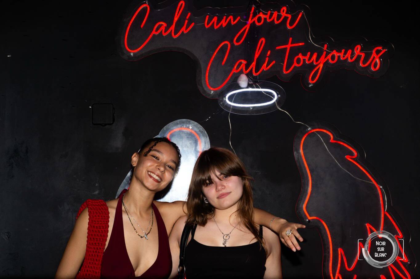 Deux étudiantes posent devant une enseigne au néon rouge indiquant « Cali un jour, Cali toujours ».